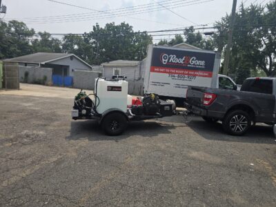 A dark grey pickup truck towing a utility trailer with a large white water tank and sewage cleaners equipment, parked in front of a Root-B-Gone service truck.